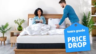 A couple laugh while lying on the Panda Hybrid Bamboo Mattress Pro on a wooden bed frame, with a blue price drop sales badge overlaid in the bottom right corner