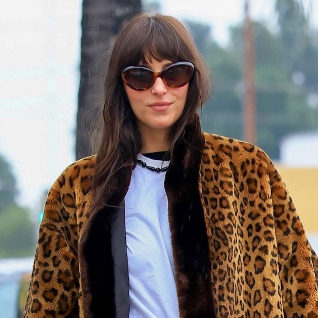Dakota Johnson wearing a leopard fur coat, white T-shirt, jeans, and patent leather Adidas Samba sneakers