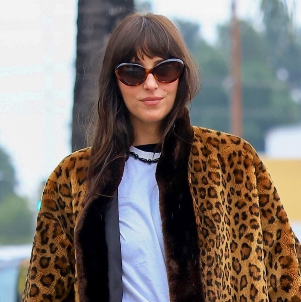 Dakota Johnson wearing a leopard fur coat, white T-shirt, jeans, and patent leather Adidas Samba sneakers