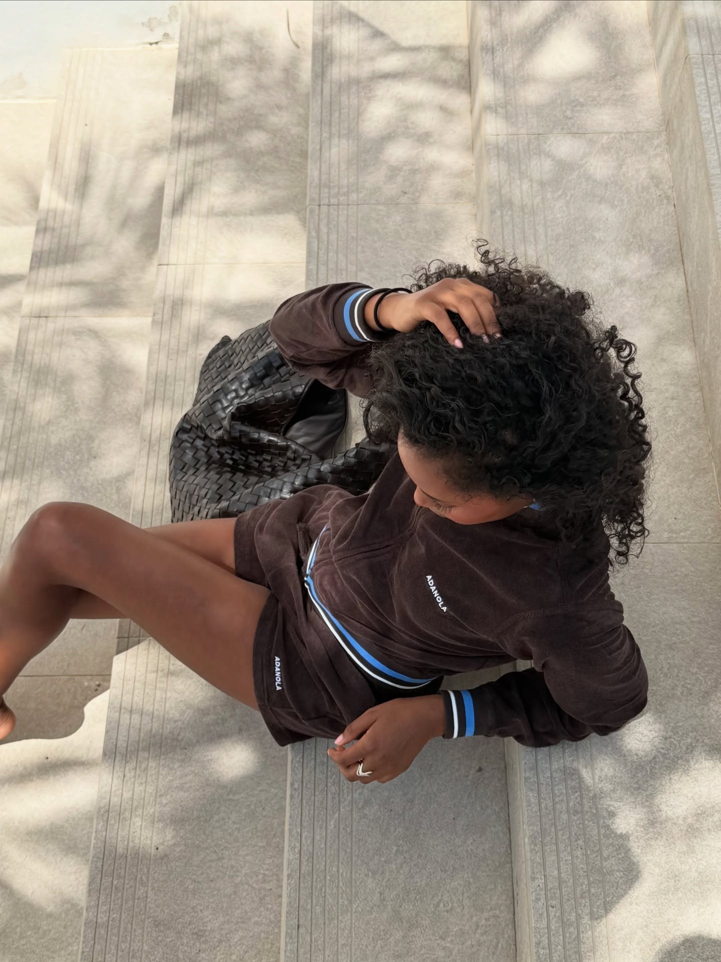 Rayan sitting on a staircase running her fingers through her curly hair.