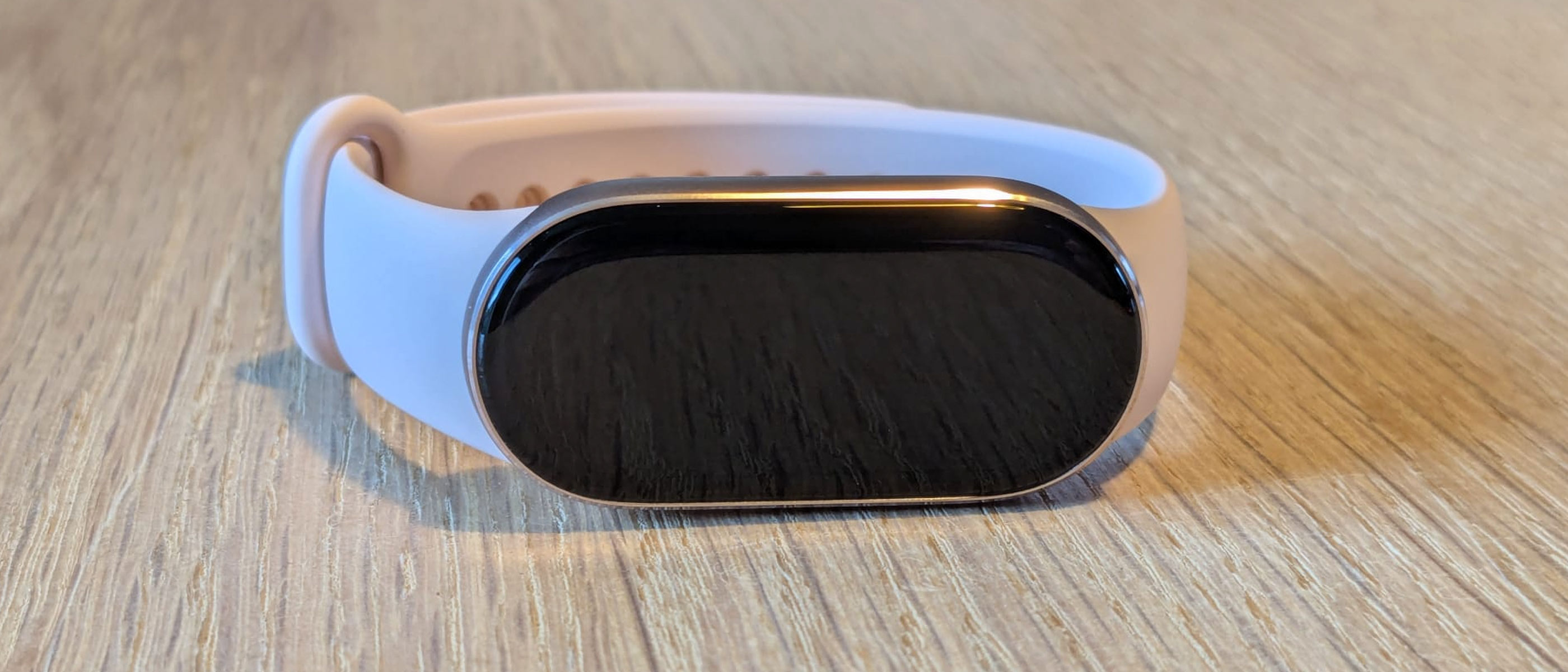 The Xiaomi Smart Band 10 with pink strap on a wooden table