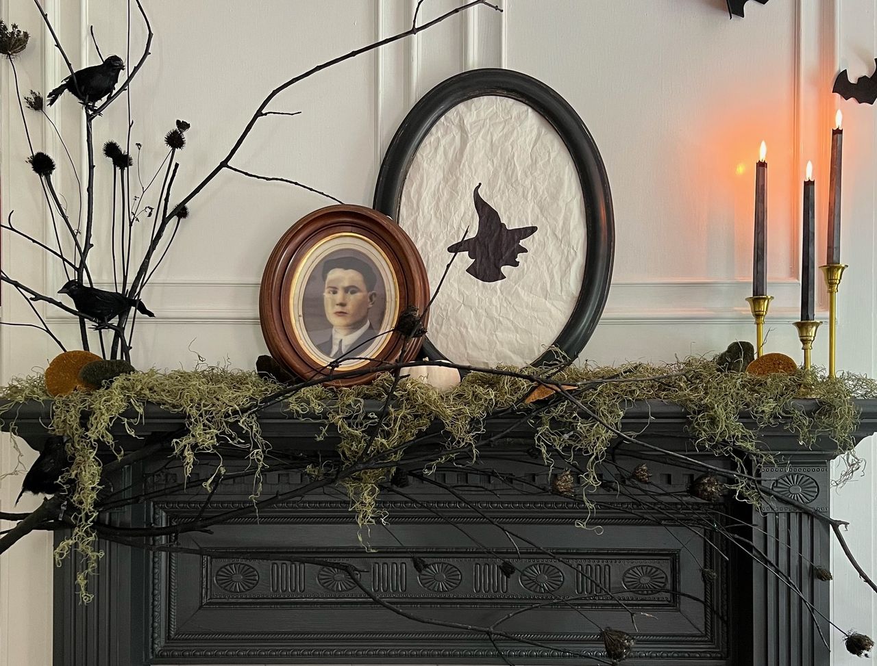 A Halloween mantel decorated with moss, witch-themed photos, and candles