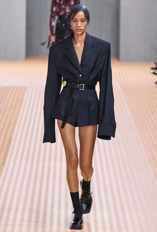 model wearing stylish outfit with socks, including a blazer tucked-in to shorts with socks and oxfords