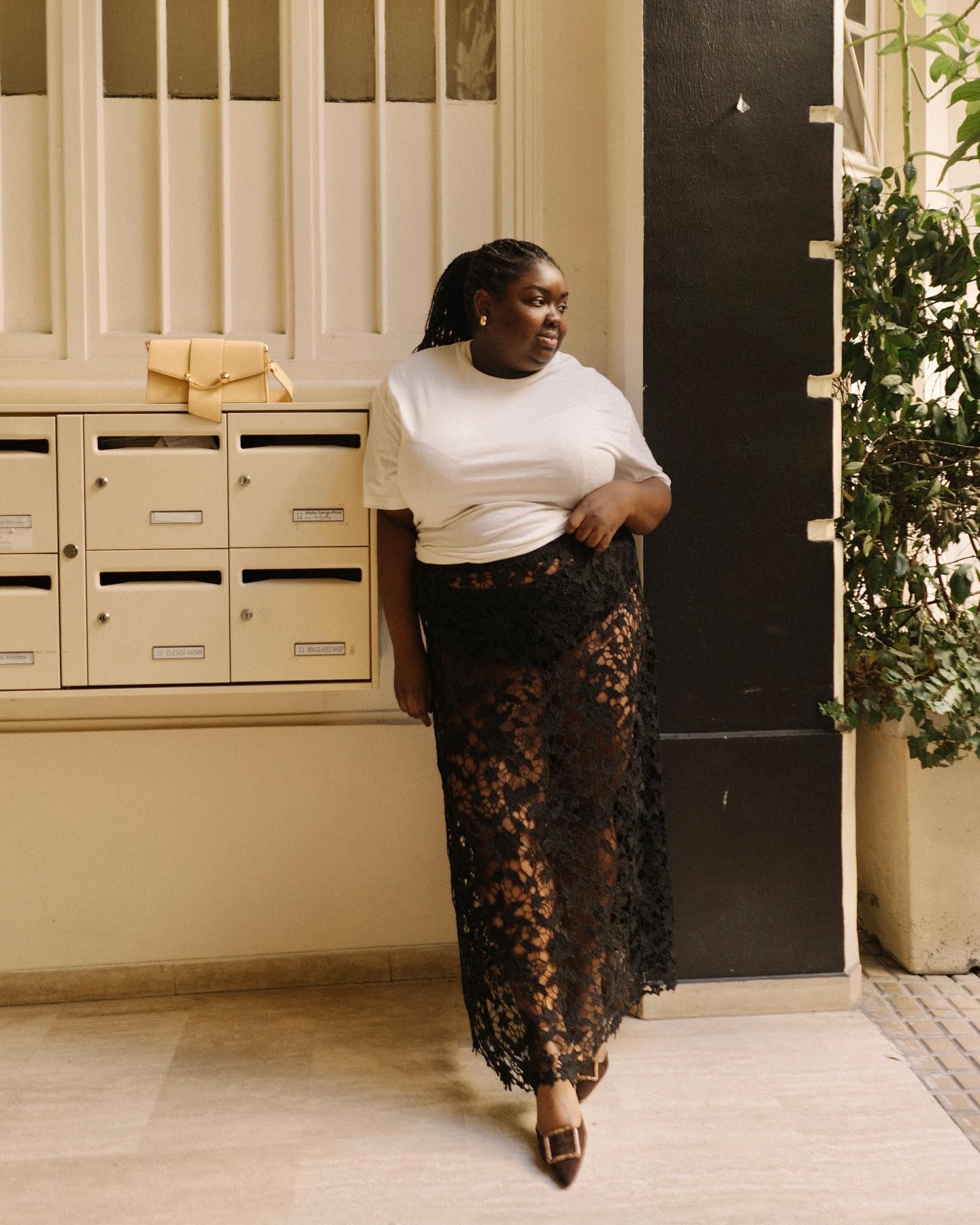 British influencer Abisola Omosole poses in a white t-shirt, sheer black lace skirt and heels