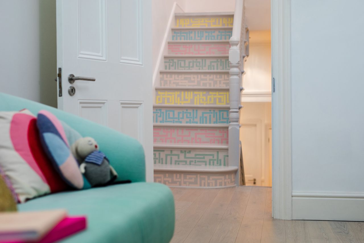 pastel painted staircase with decorative multi-colored pattern, leading on from the living room, with a green sofa and multi-colored cushions