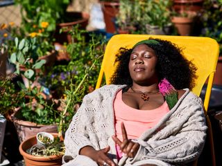 A woman sleeps in a lounge chair surrounded by plants