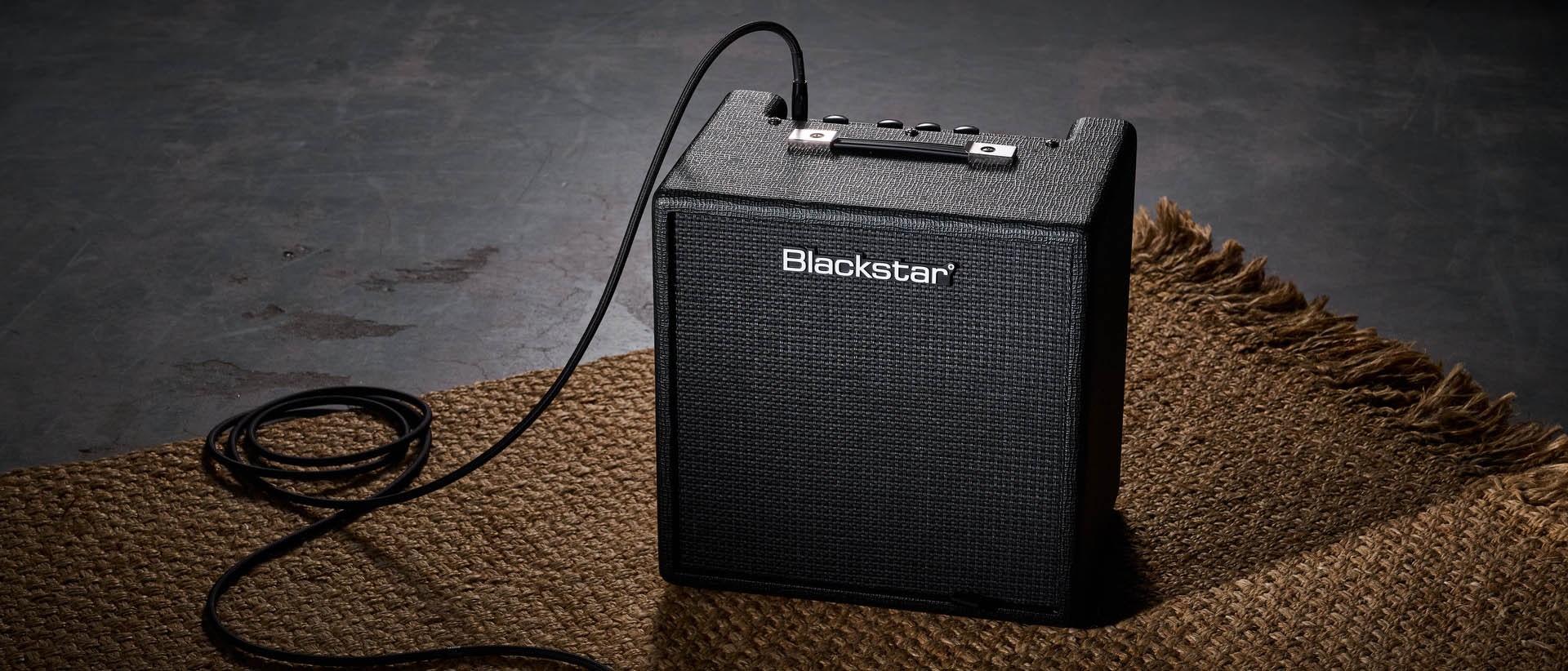 Blackstar Debut Bass 25: this compact little combo is finished in black with matching grille clothe and is photographed in close-up against a stone floor and weaved rug.