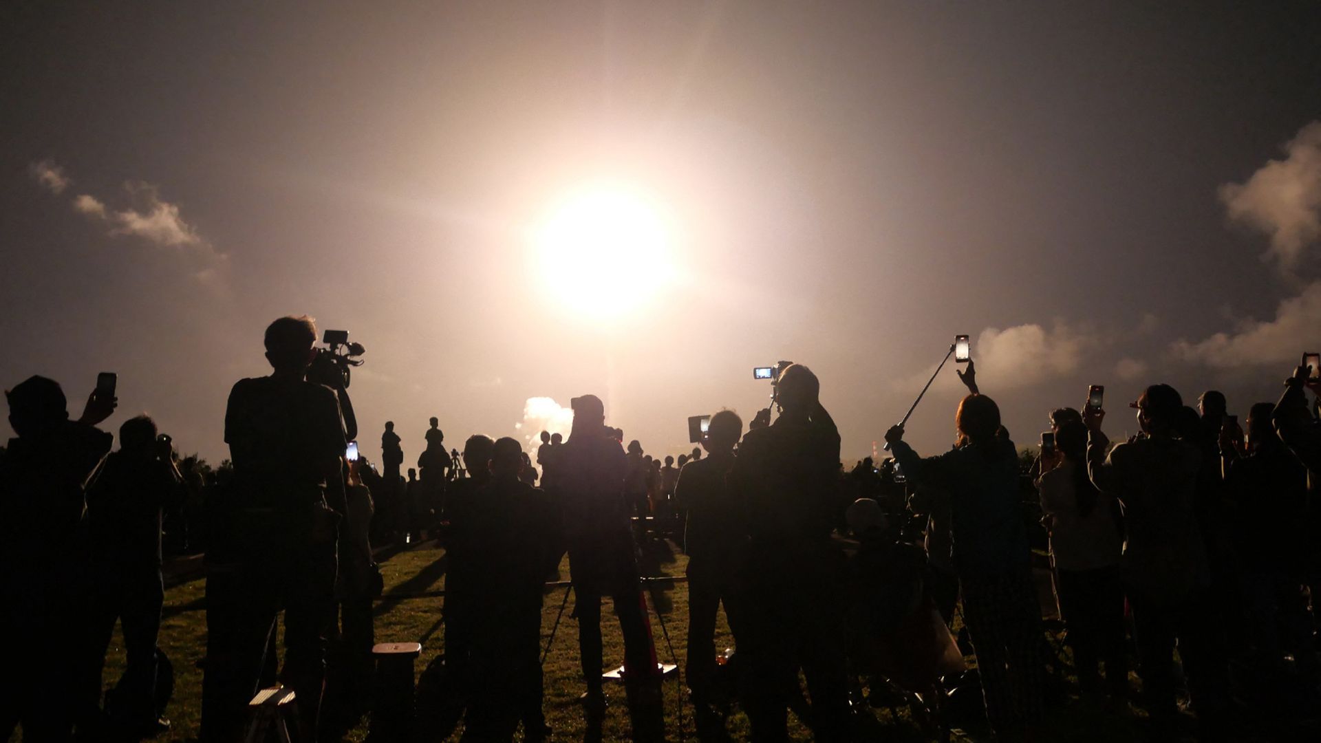 A photo of a crowd watching a rocket launch at night