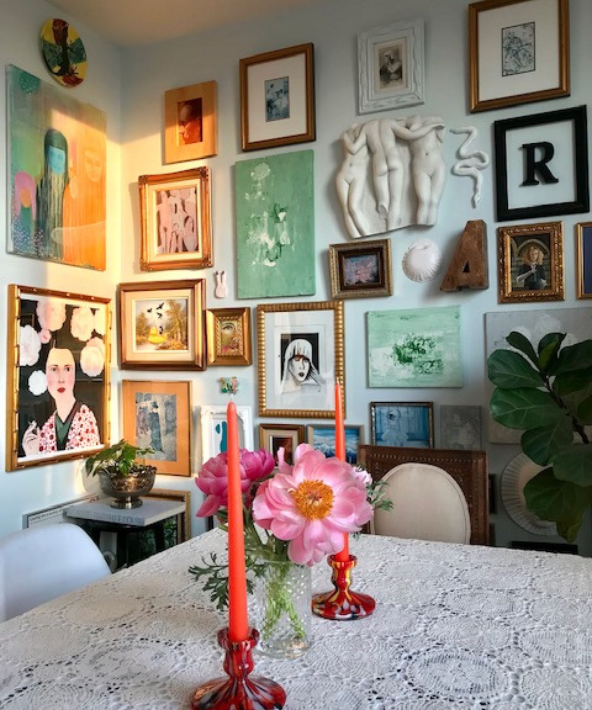 Gallery wall with a mix of pictures and prints beside table with vintage tablecloth and candles