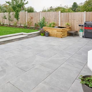 Large grey patio area with raised grass and plant beds next to it