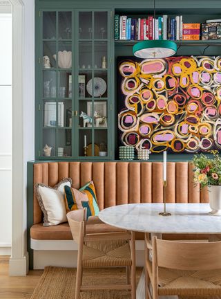 Breakfast room with green painted fitted cabinets, colorful art and banquette seating