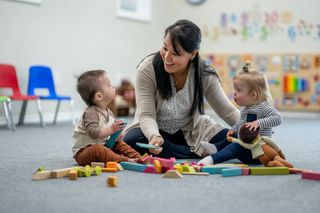 Care worker sitting on the floor with two toddlers at nursery playing with toys