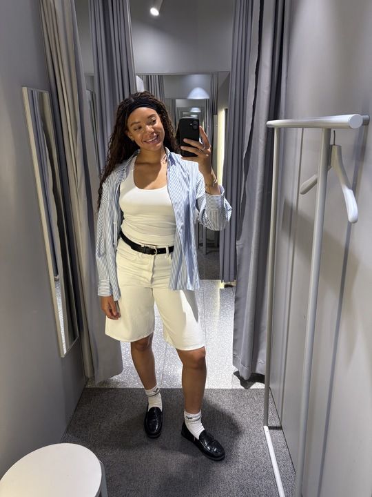 junior fashion editor Imani wears the Arket white denim Bermuda shorts with a white tank stripped shirt and black belt in the Arket changing rooms in a image taken recently.