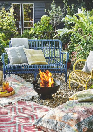 small metal fire pit in garden with blue bench and cushions