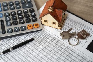 Calculator, model of a house and front door keys sitting on top of some paperwork