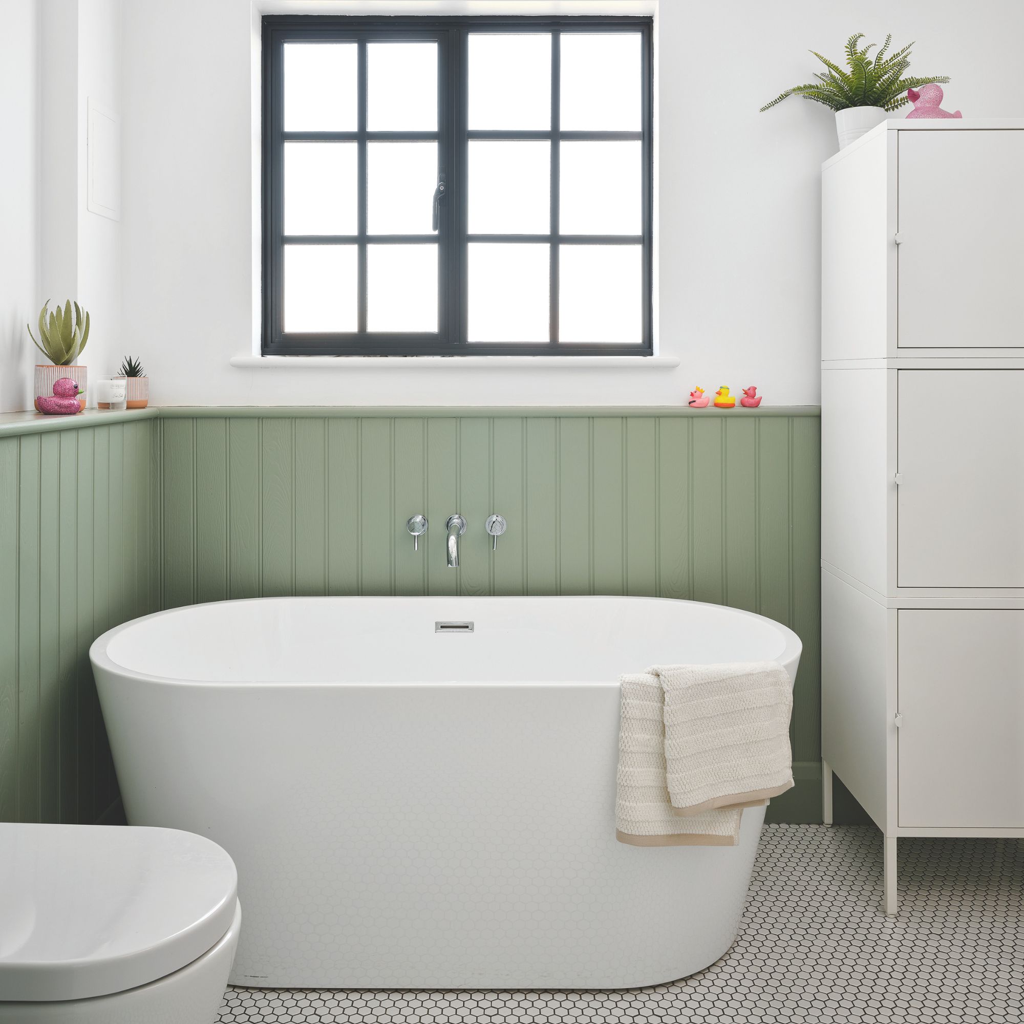 White painted bathroom with green wall panelling and a freestanding bath