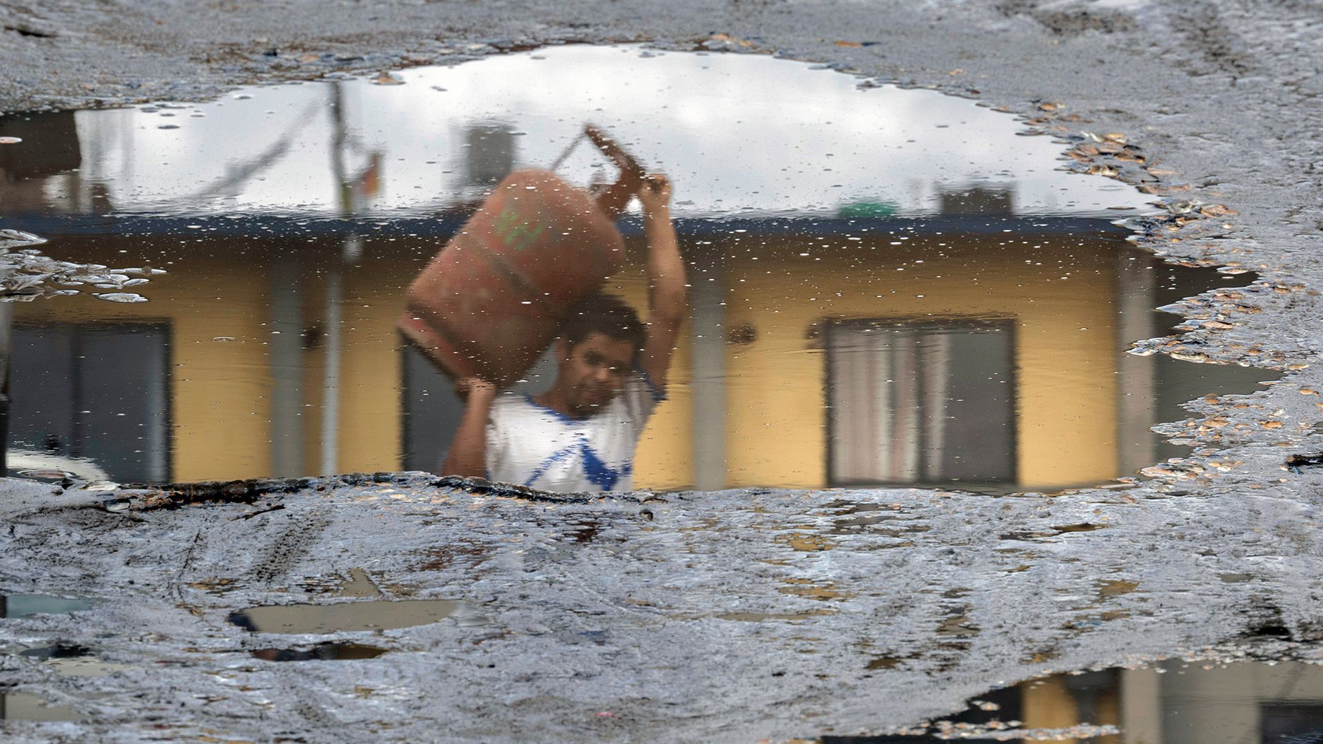 
                                A person reflected in a puddle carries an empty LPG cooking gas cylinder during a gas shortage in Kathmandu, Nepal
                            