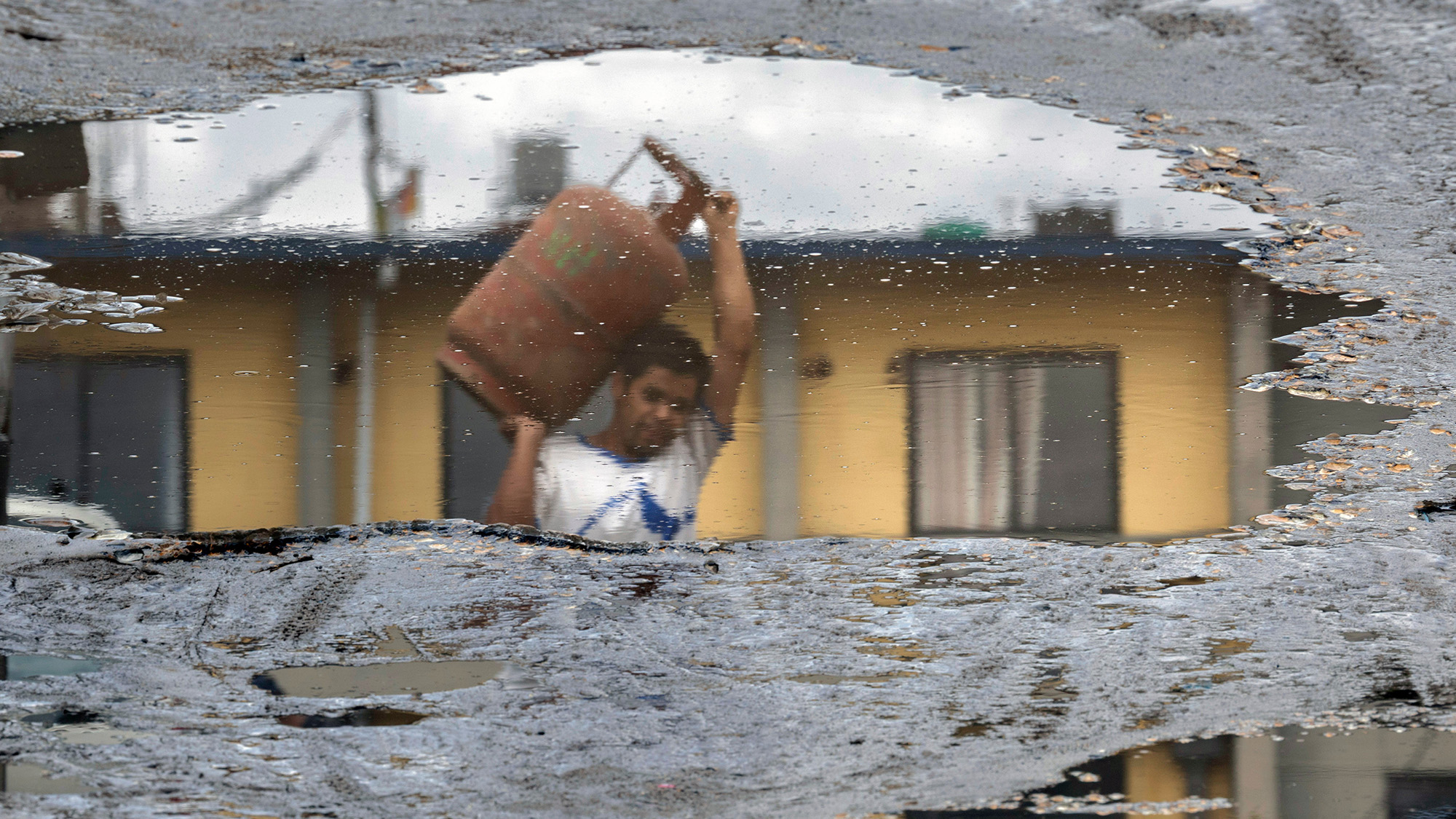 A person reflected in a puddle carries an empty LPG cooking gas cylinder during a gas shortage in Kathmandu, Nepal