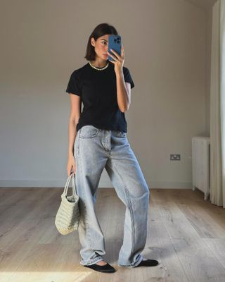 Woman wearing baggy light wash jeans with black t-shirt and black ballet flats.