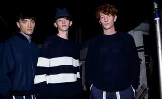 Three guys wearing E Tauts S/S 2015 collection. The guy on the left is wearing a blue shirt, navy jacket and white and navy striped pants. The guy in the middle is wearing a knitted navy jersey with 2 white stripes and the guy on the right is wearing a navy jersey and a navy and white striped pants