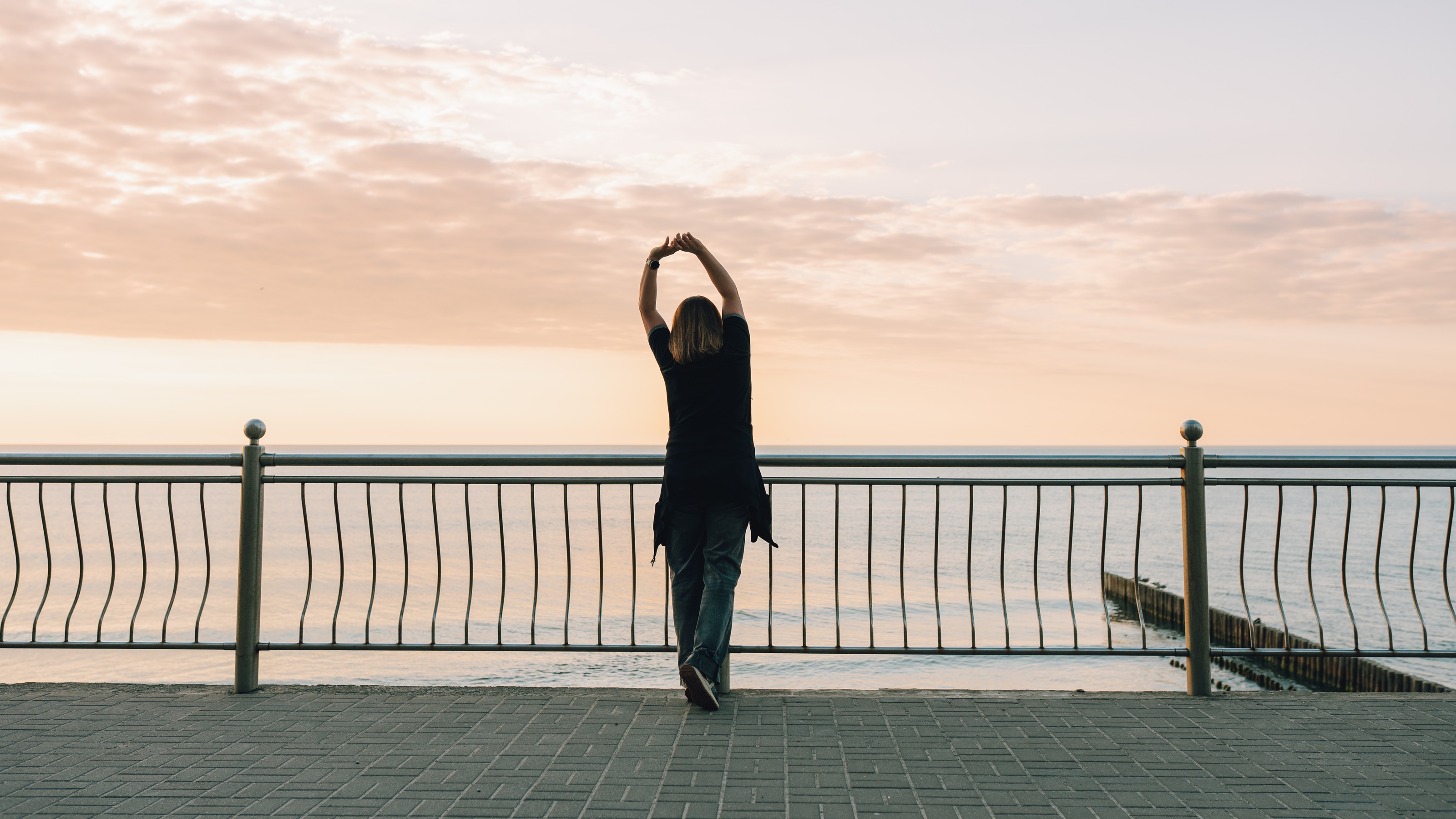 A woman stretches on a promenade by the sea at sunrise.