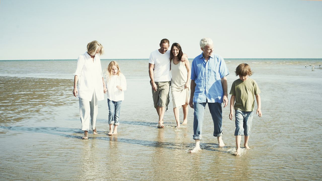 A multigenerational family walks together on the beach.