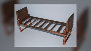 This image shows the recreation of a bronze bed which was found by archaeologists in Greece. It is plain looking, and has a rectangular bronze headboard on both ends. It has several wooden slats. The legs are made out of several knobbly bits of bronze, but nothing intricate.