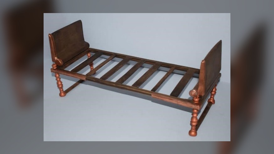 This image shows the reconstruction of a bronze bed discovered by archaeologists in Greece.  It is simple and has a rectangular bronze headboard at both ends.  It has several wooden slats.  The legs are made of several pieces of knotted bronze, but nothing complex.