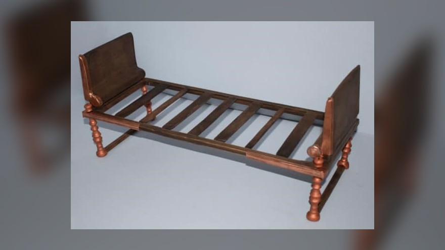 This image shows the recreation of a bronze bed which was found by archaeologists in Greece. It is plain looking, and has a rectangular bronze headboard on both ends. It has several wooden slats. The legs are made out of several knobbly bits of bronze, but nothing intricate.