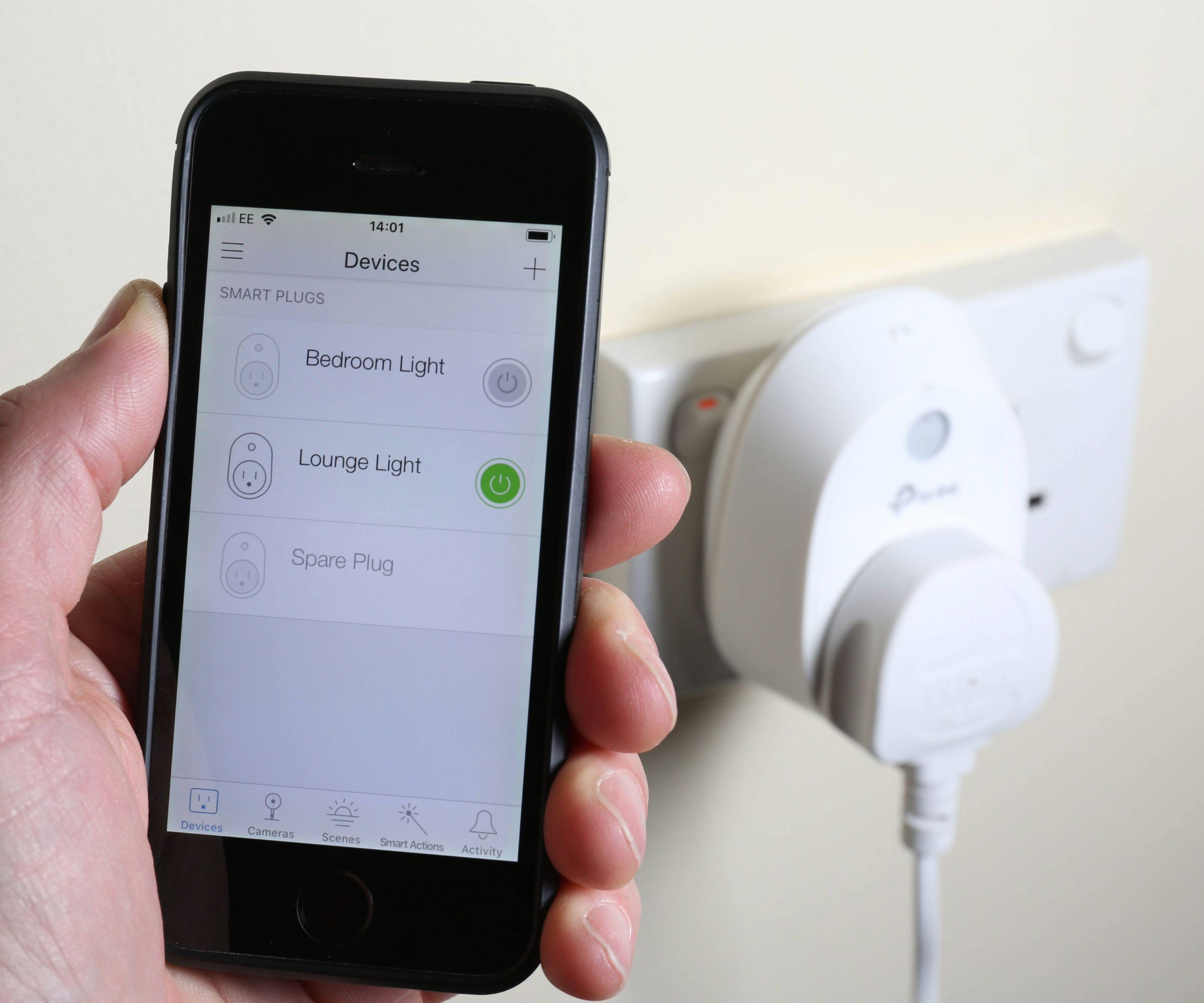 Hand holding up a smart phone with smart plug behind