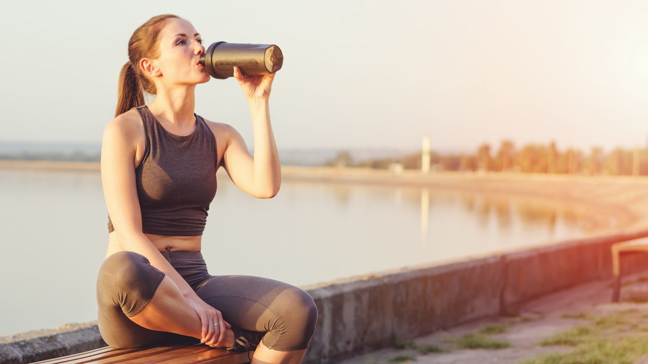 Young girl running after sitting on the bench. Sportswoman drinks from the shaker.