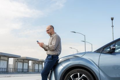 A man leans against his car while using his smartphone.