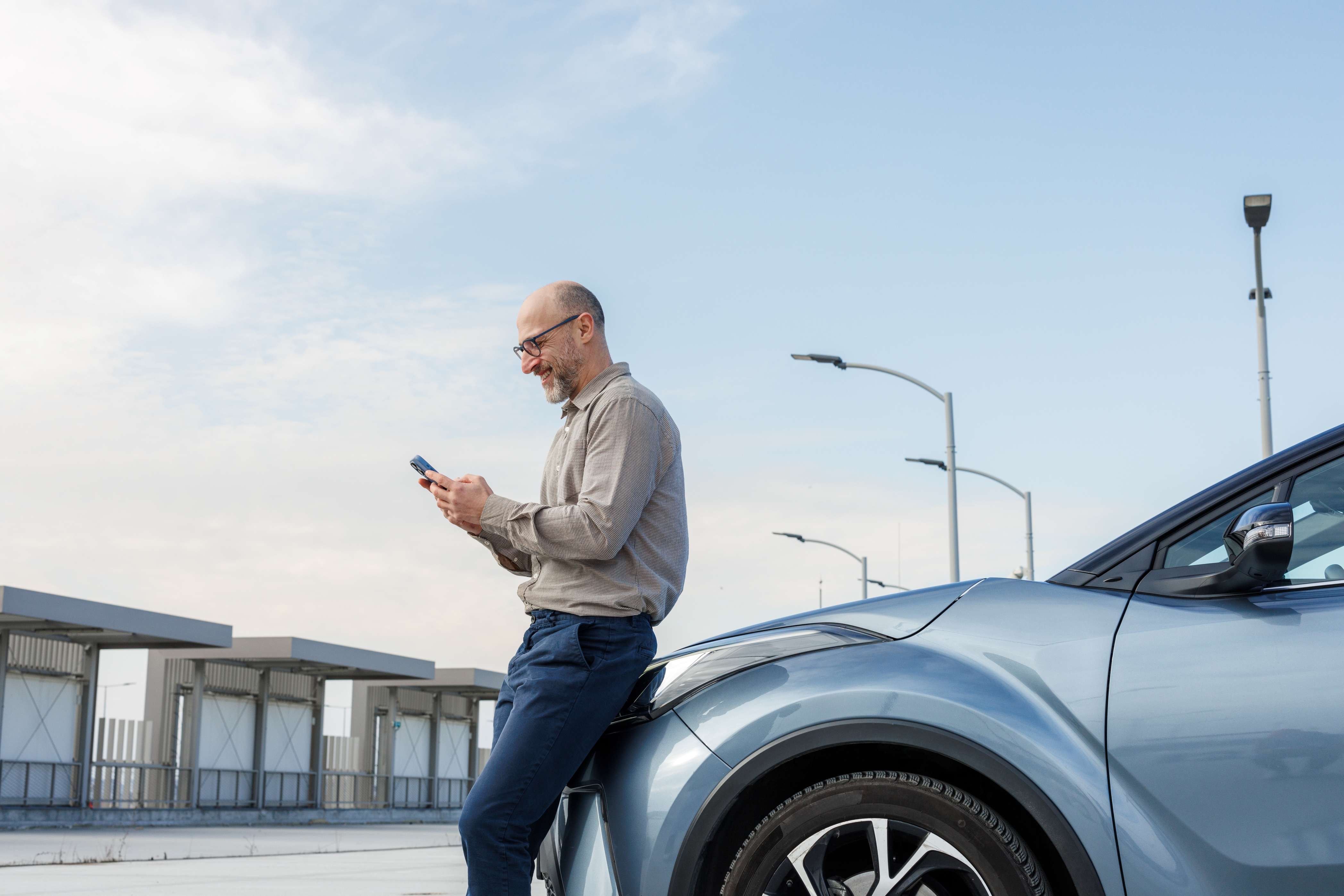A man leans against his car while using his smartphone.