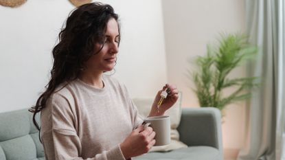 woman adding drops of a supplement to her coffee