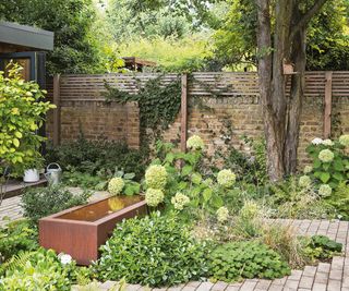 A corten steel water feature in a small bricked garden