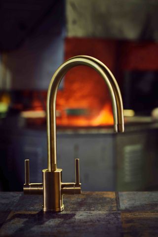 Close up of a brass tap on a rustic tiled worktop, blurred image of a fired kiln in the background