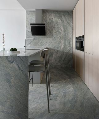 A stone drenched kitchen with gray stone on the walls, floor, and island paired with wood cabinets