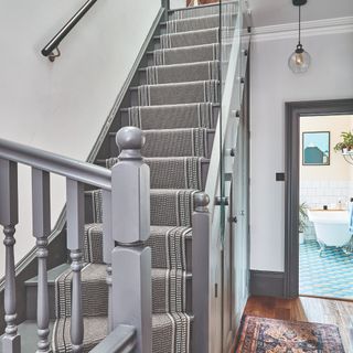 A grey staircase with a patterned black and white runner rug in a hallway