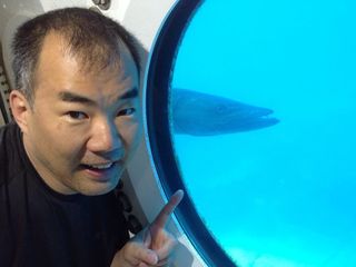 JAXA astronaut Soichi Noguchi in the Aquarius underwater laboratory, with a barracuda in the background. Noguchi was on the SEATEST crew that worked in the lab in September 2013.