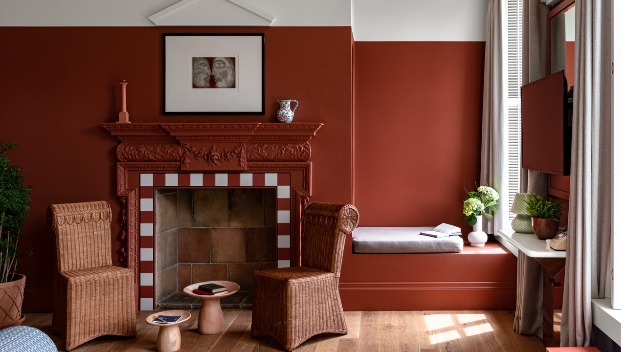 Cowley Manor, fiery red wall and fireplace surround with two wicker chairs and abstract artwork above