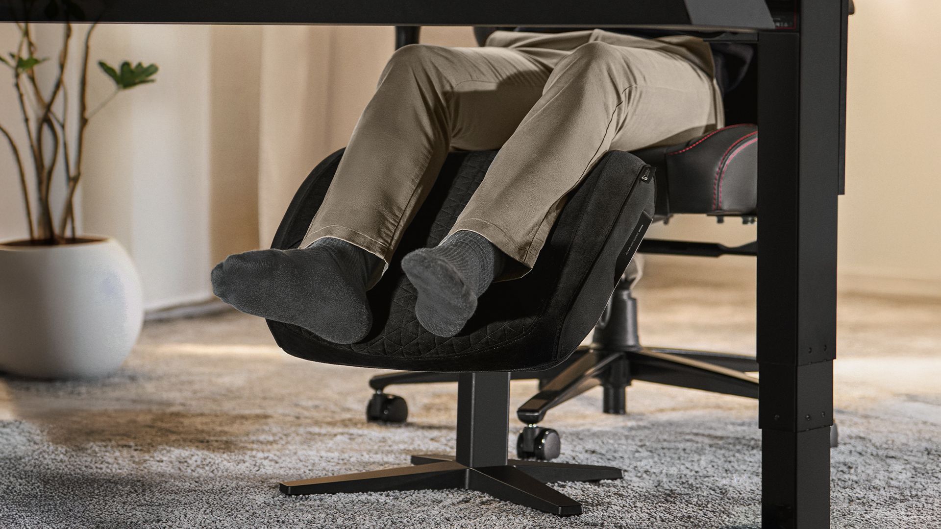 An under-desk shot showing a man's legs lifted up by the Secretlab OTTO Adjustable Legrest