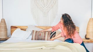 Woman placing a pillow on a made bed with lots of layers of bedding