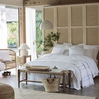 Neutral colored bedroom with white linen bed, green plants and woven accessories
