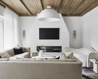 Living room with white walls, beige sectional and white sofa, fireplace, large pendant light and wall lights