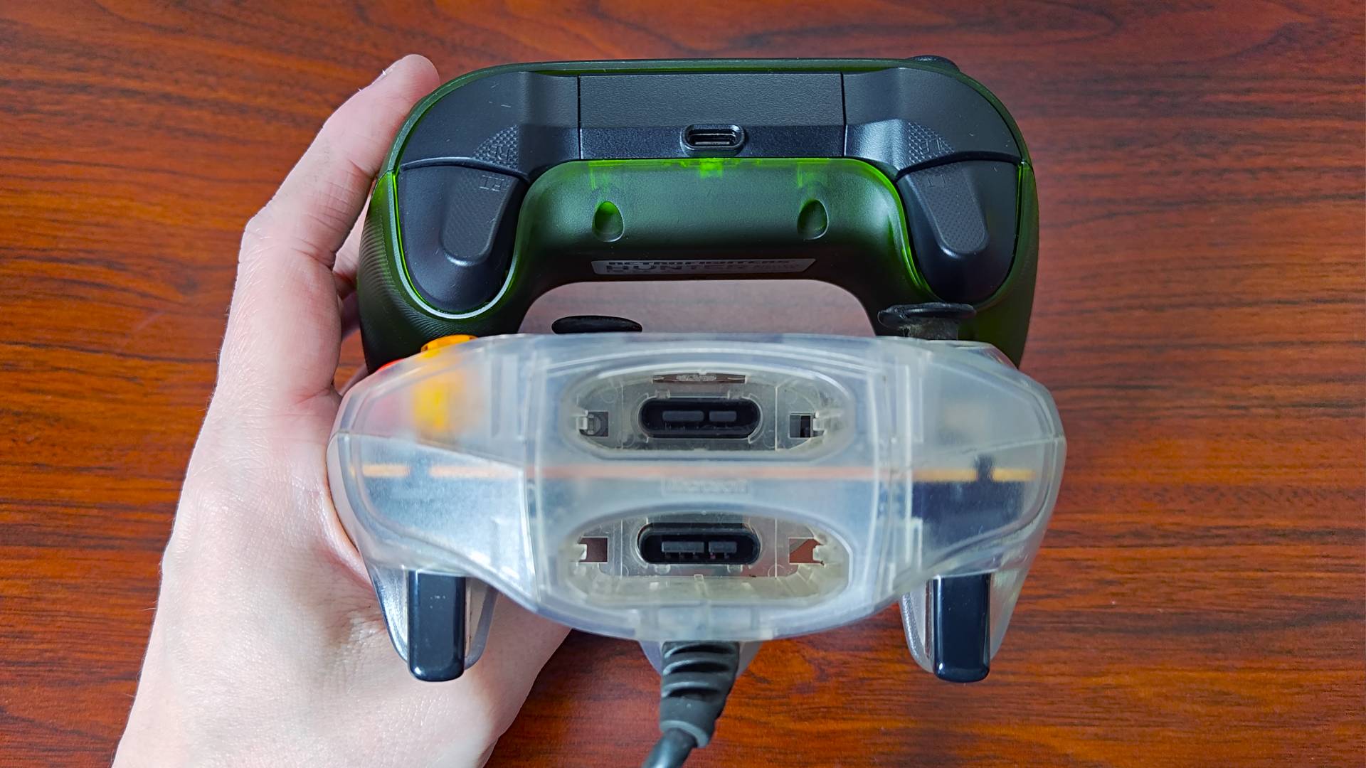 Hand holding Retro Fighters Hunter and white transparent OG Xbox S controller next to woodgrain desk to show memory card slots.