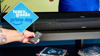 the bose smart soundbar with a panasonic TV and a hand holding the remote and pointing it at the TV with a tom's guide blue diamond deals badge