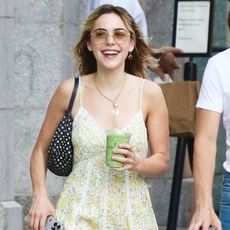 Kiernan Shipka smiles wearing a floral sundress and a black shoulder bag