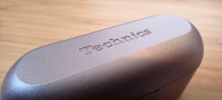 A pair of silver Technics EAH-AZ40M2 earphones on a wooden table