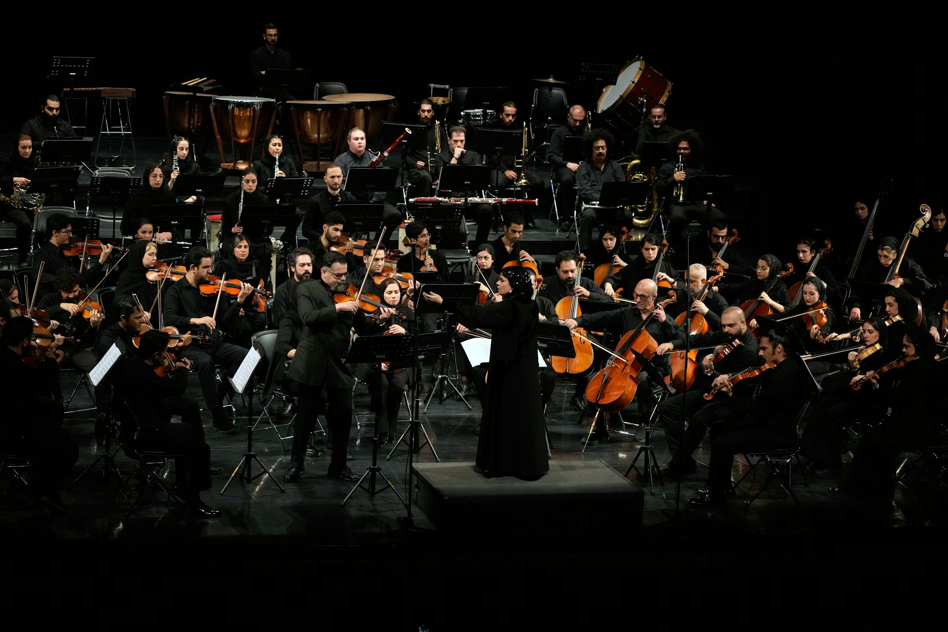 An orchestra conductor monitoring and directing an ensemble of musicians.
