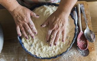 Woman patting crumble mixture into a pie dish, making a fruit crumble pudding.